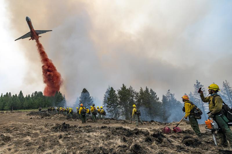 Firefighters watch and take video with their cellphones as a plane drops fire retardant on Harlow Ridge above the Lick Creek Fire, southwest of Asotin, Wash., on July 12, 2021. The fire, which started last Wednesday, has burned over 50,000 acres of land between Asotin County and Garfield County in southeast Washington. CREDIT: Pete Caster/Lewiston Tribune via AP