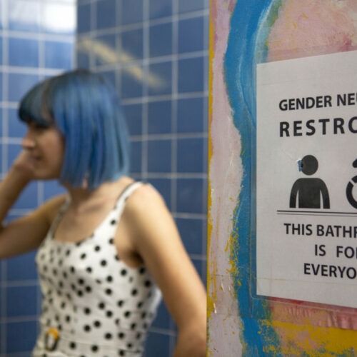 A nonbinary person next to gender-neutral sign to a bathroom. Photo by Zackary Drucker/Broadly’s Gender Spectrum Collection