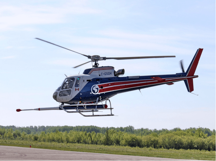 Helicopter in mid-air with equipment underneath to survey the land for cobalt. 