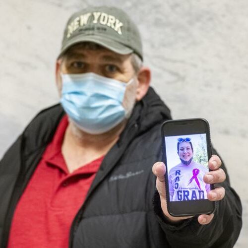 Man in mask holding up cell phone with image of his deceased daughter