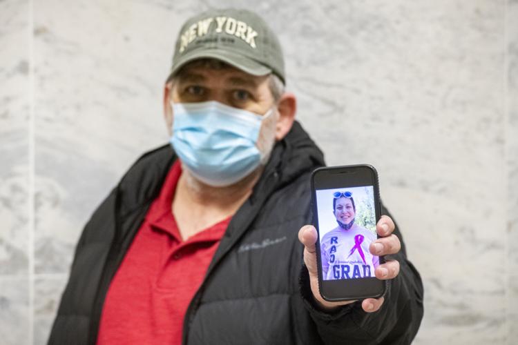Man in mask holding up cell phone with image of his deceased daughter