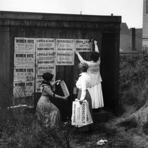 Black and white photo of three women putting up signs about Women's voting rights.