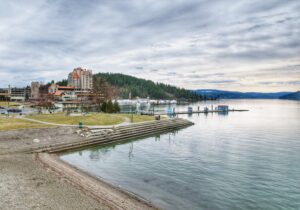 A sandy beach and park near Lake Coeur d'Alene are covered by grey skies.