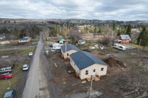 Newly constructed houses sit atop a hill of brown mud surrounded by rolling hills and trees.