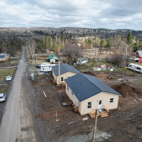 Newly constructed houses sit atop a hill of brown mud surrounded by rolling hills and trees.