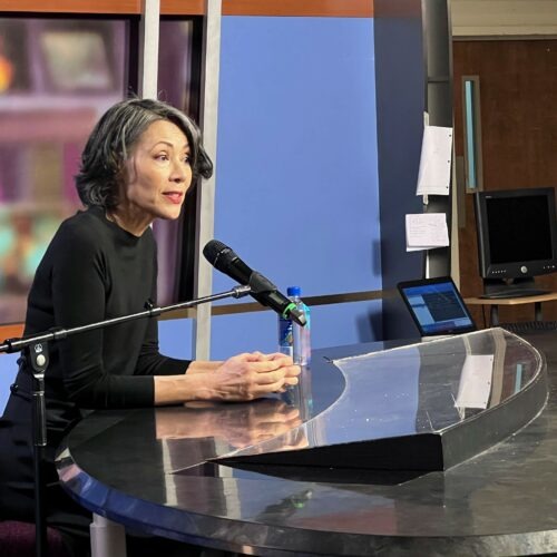Journalist Ann Curry sitting behind a student anchor desk talking about reporting.