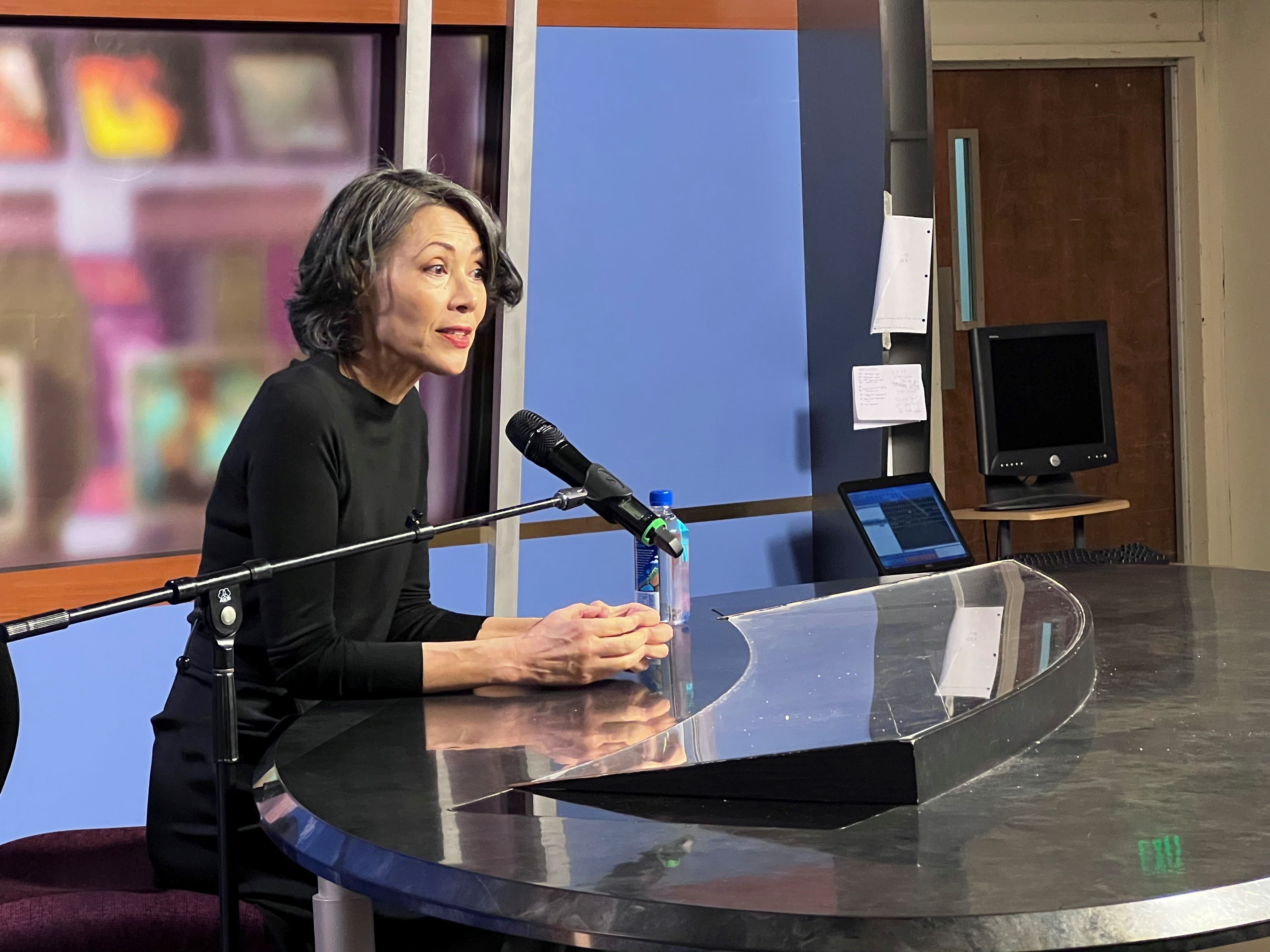 Journalist Ann Curry sitting behind a student anchor desk talking about reporting.