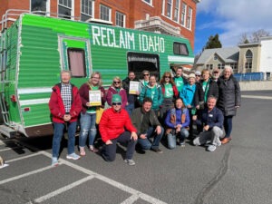 A group of Reclaim Idaho volunteers pose together in front of the big green Reclaim Idaho camper van.