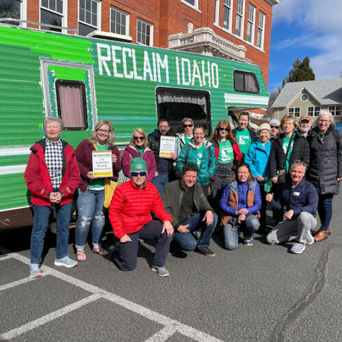 A group of Reclaim Idaho volunteers pose together in front of the big green Reclaim Idaho camper van.
