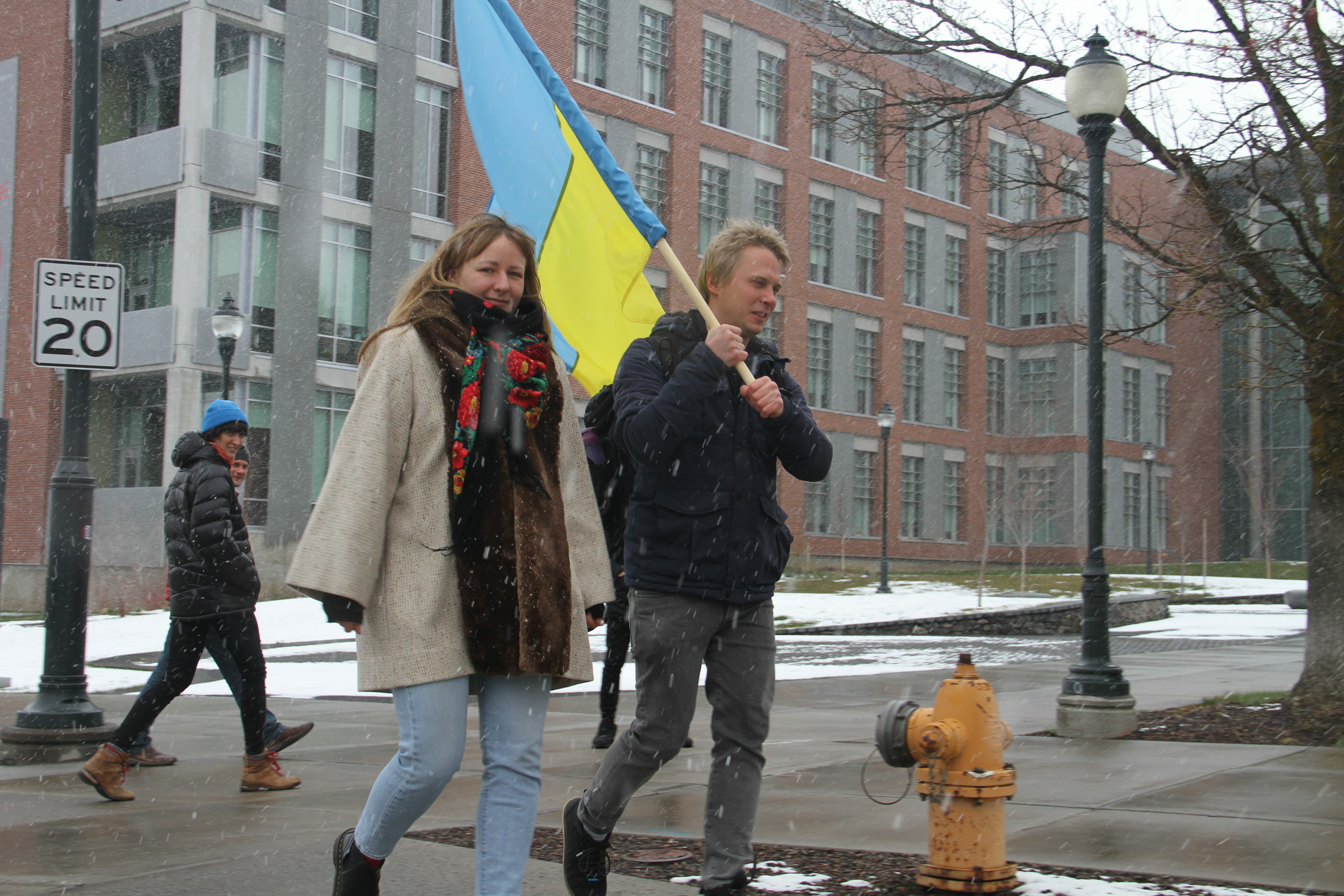 Two blondes carry a Ukrainian flag across the WSU Pullman campus as snow lightly falls.
