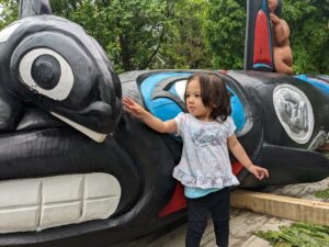 A young toddler touches the head of a black and white carved Orca.