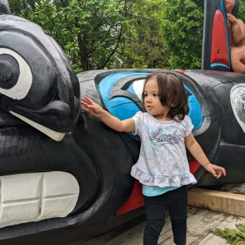A young toddler touches the head of a black and white carved Orca.