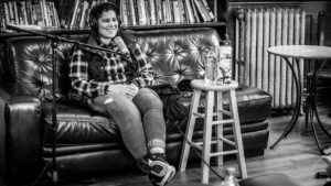 Wide shot of the recording setup in Washington Hall. Nikita sits on a couch, with a microphone in front of them. Two water bottles sit on top of a stool to their left.