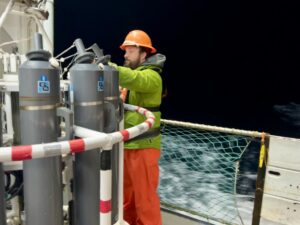 Jonathan Witmer, a survey technician with NOAA, readies equipment for the scientists as waves crash against the side of the ship.