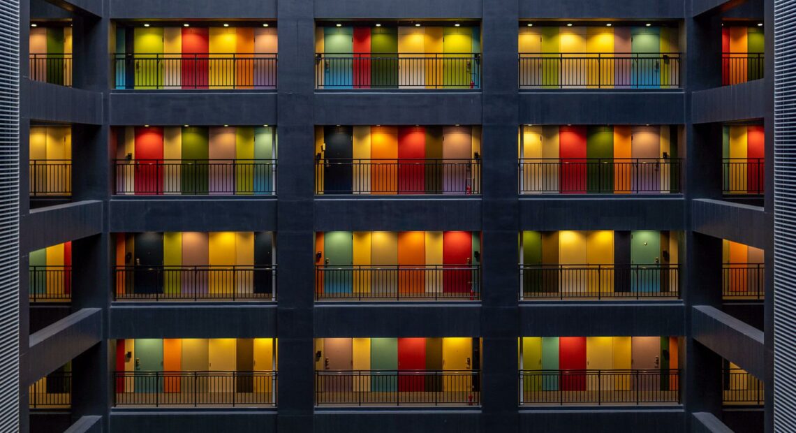 Apartments with colored walls are dimly lit from far away under evening light.