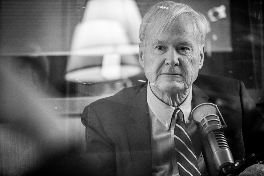 Chris Matthews wears a serious expression on his face. His microphone is positioned in front of him. There is a thin film glare across the photo because it was shot from outside the recording studio.