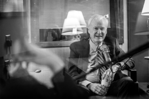 We see Sueann Ramella's hand on the left-side foreground of the image. On the right-side middle-ground Chris Matthews smiles and laughs while answering a question. He holds a cup of coffee in his hands.