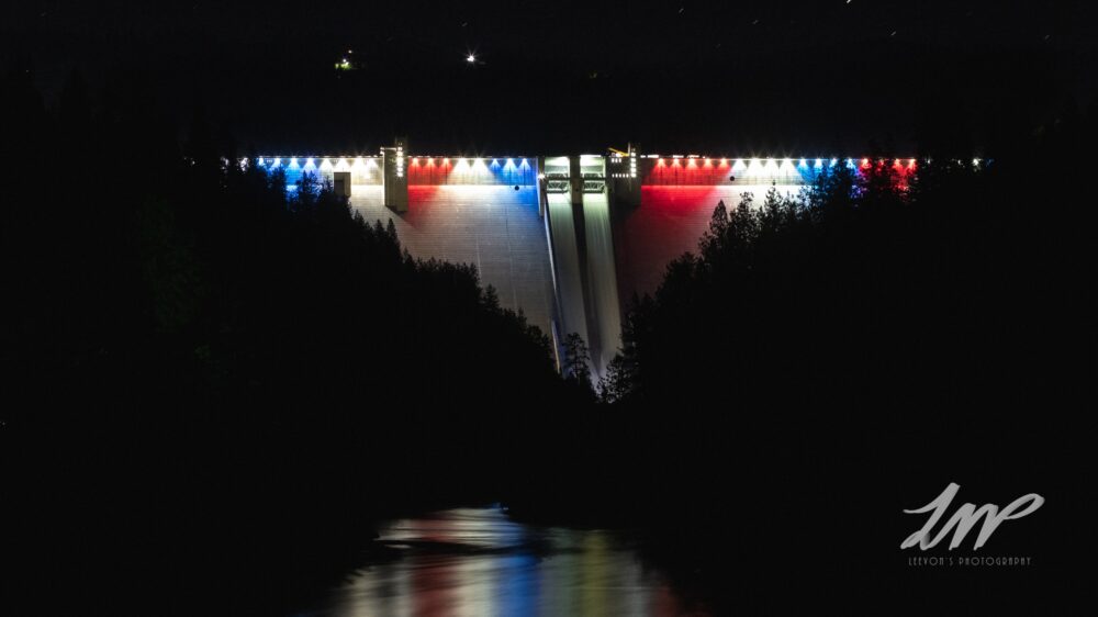 The Dworshak Dam glows red white and blue surrounded by the black of night.