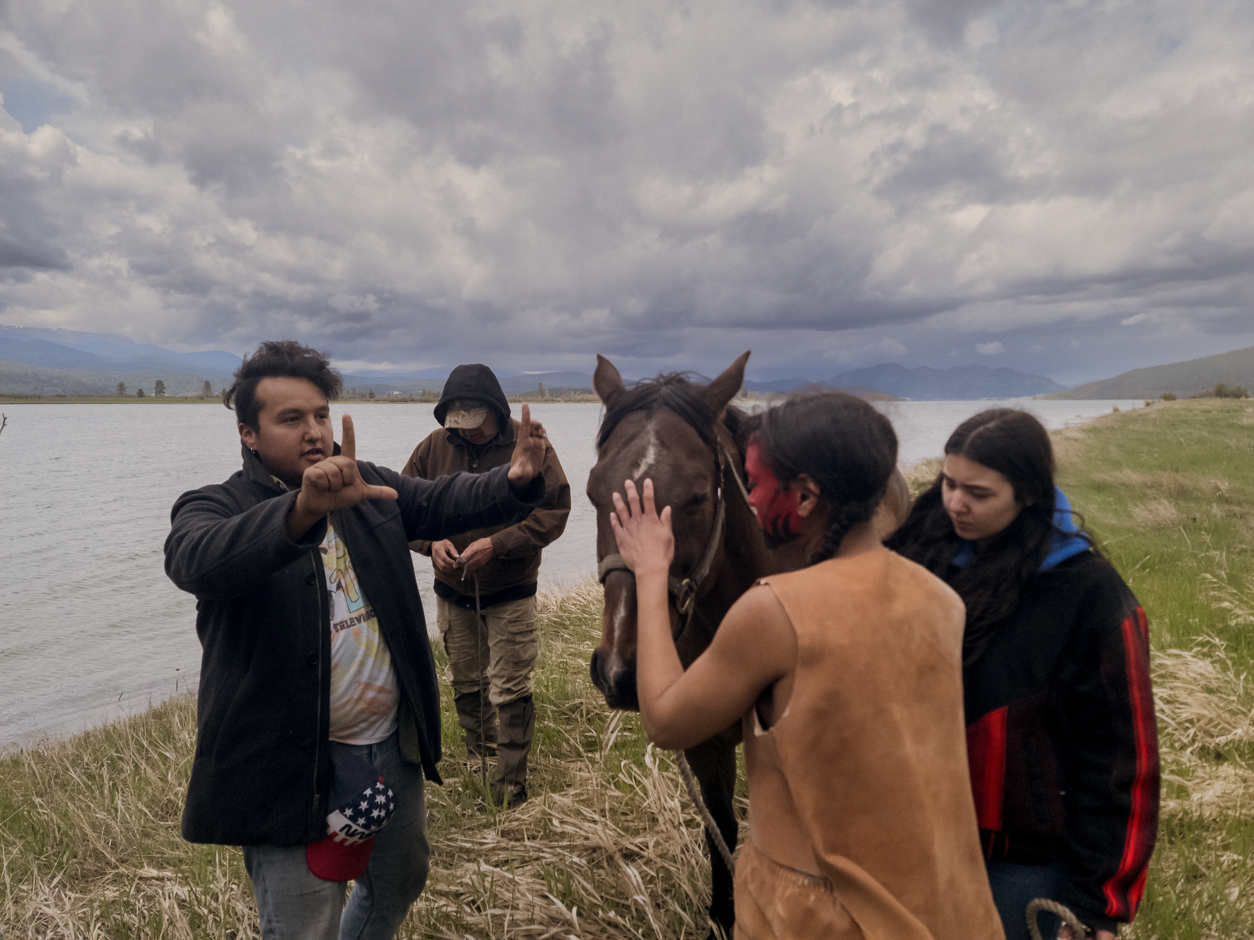 Cast and crew stand on the shores of the Spokane River next to a brown horse.