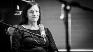 Sarah Zabel sits in front of a microphone and smiles. She seems like she is listening.