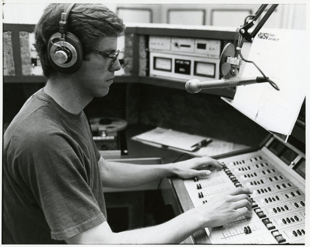 Bill Morelock sits in front od a sound board and microphone,