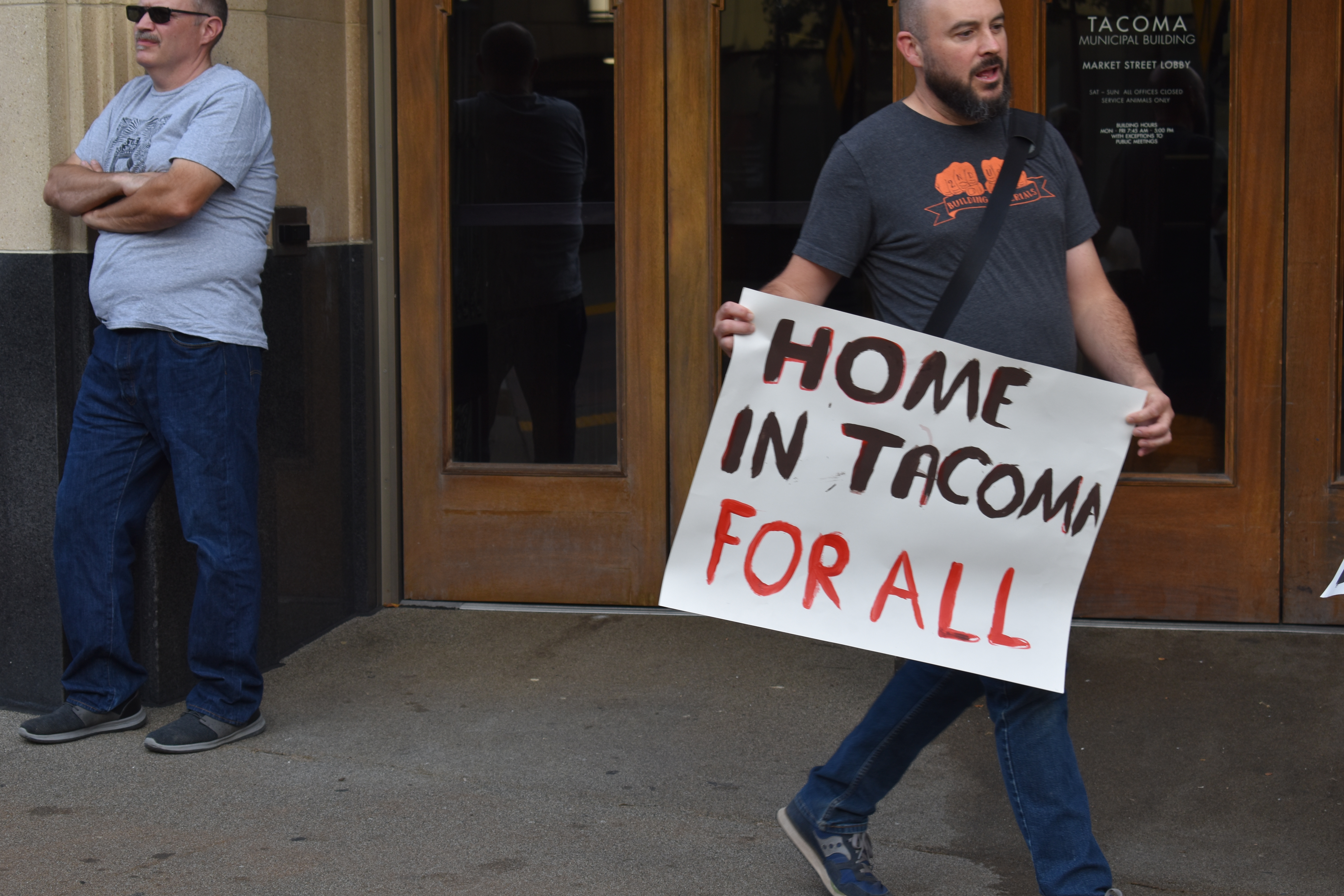 Ty Moore, with the Tacoma & Pierce County Democratic Socialists of America, holds a sign in support of Home in Tacoma For All at a rally for housing justice outside the city municipal building. Photo by Lauren Gallup.