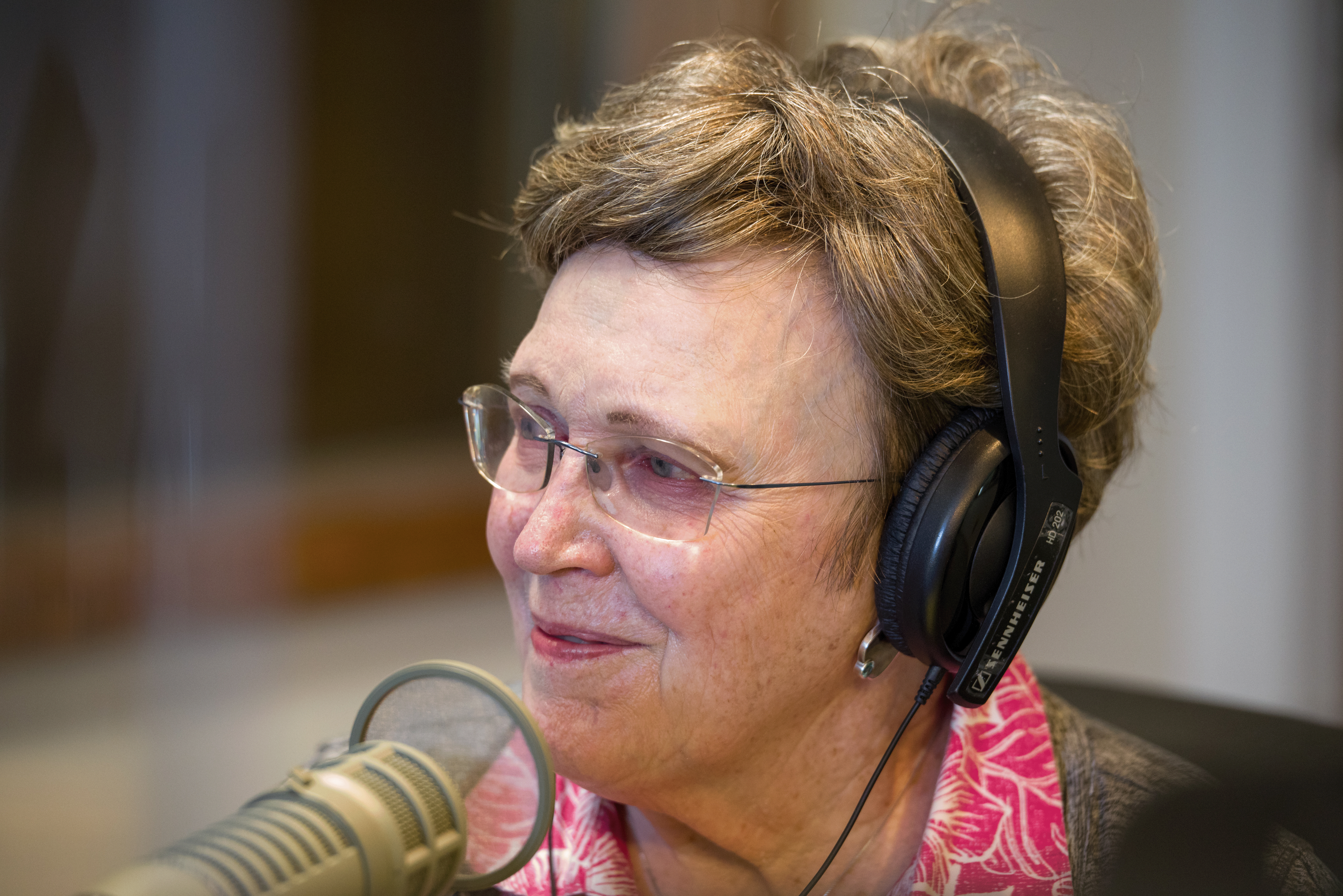 This is a present day photo of Nancy Mack. She is smiling and talking into a microphone. She wears a pink shirt.