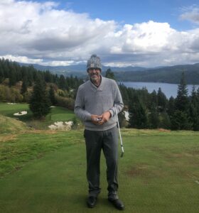 Bill Morelock on a golfing green. He stands in the center of the photo smiling.