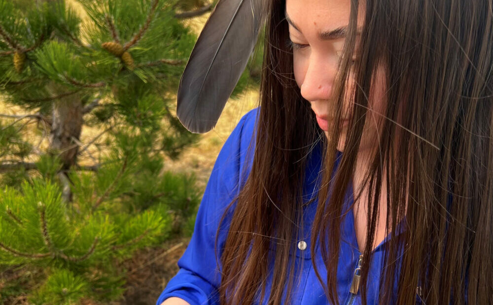 A young Native American girl with long black hair and a bright blue shirt holds a mobile phone with the Camp Crier app.
