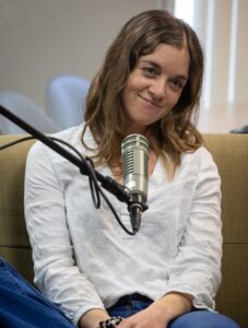 This is a photo of podcast guest Emerald LaFortune. She smiles in front of a microphone.