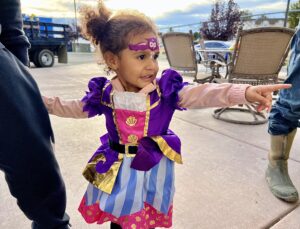 A little girl in a princess dress points to the right.