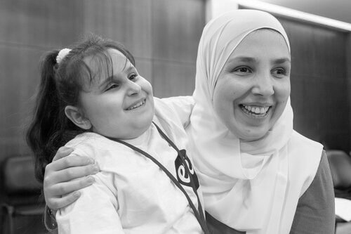This is a black and white photo of Sara Minkara and a young girl embracing and smiling together. The young girl is a participant of ETI's program.