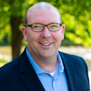 white man in blue shirt with black glasses