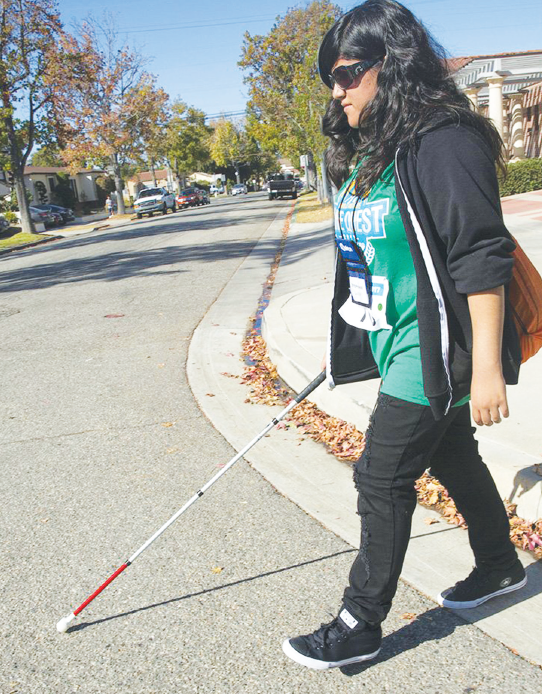 young teen with a visual impairment walks down a street with a cane.