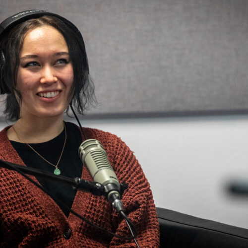 Podcast guest Zoe Hana Mikuta sits in front of a microphone and smiles.