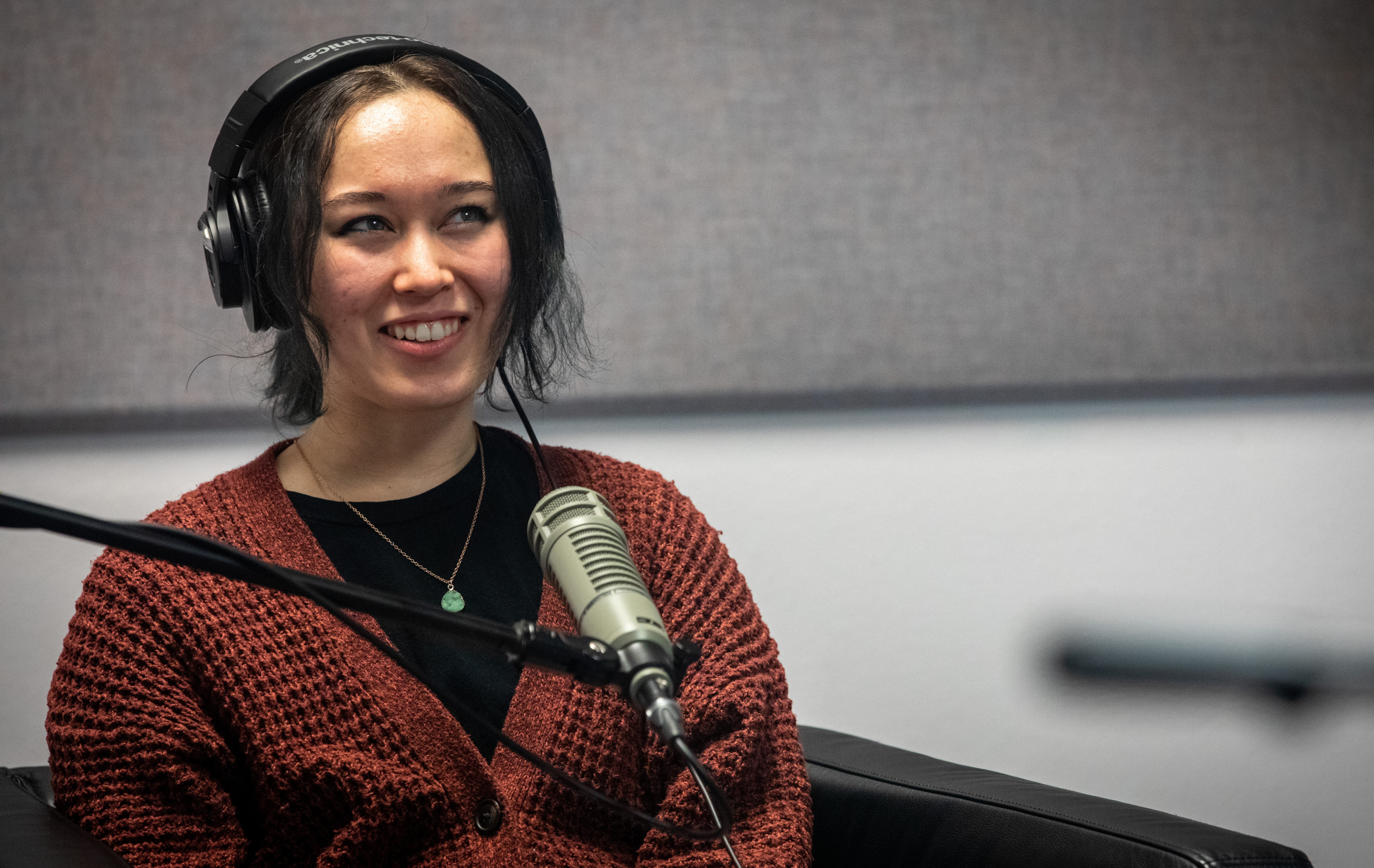 Podcast guest Zoe Hana Mikuta sits in front of a microphone and smiles.