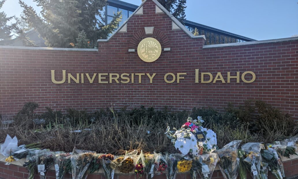 Bouquets of flowers are set out in front of a brick sign that reads "University of Idaho."