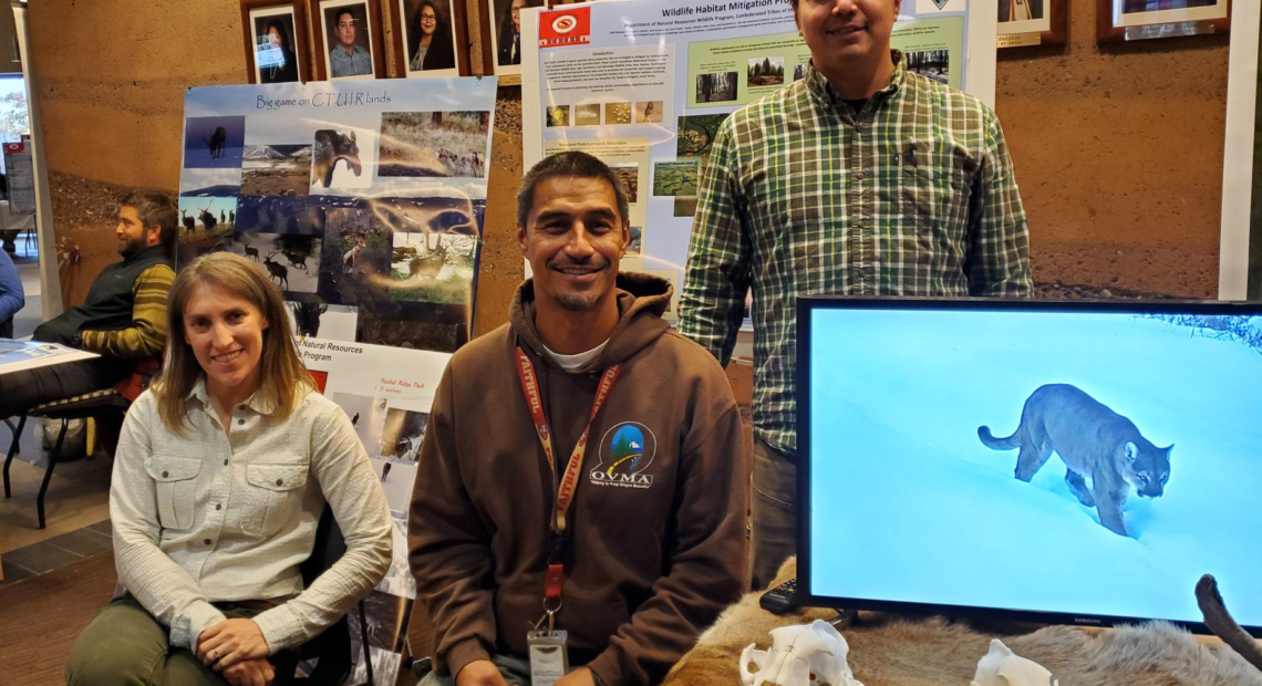 a white woman and two Native men sitting behind a display of skulls