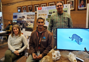 a white woman and two Native men sitting behind a display of skulls