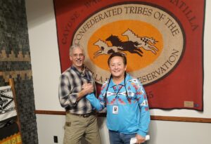 white man grasping the hand of a Native man in from of a large flag