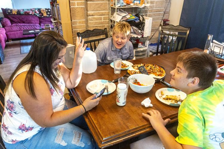 A mom and two sons sit at a table and eat a meal together. They are laughing. 