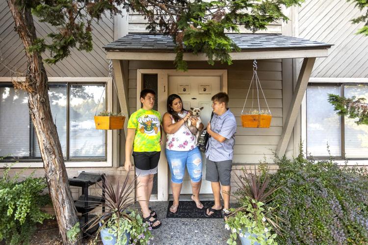 A mom and two sones stand in front of their rental home. She is holding a small dog.