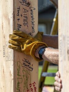 Construction worker with gloved hand holding wood beam with people's names written on it.