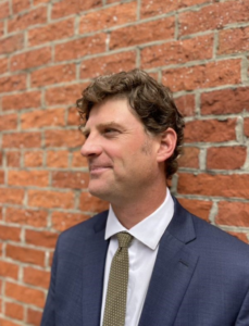 Brian Points is President of Points Consulting standing by a brick wall in a suite and tie. 