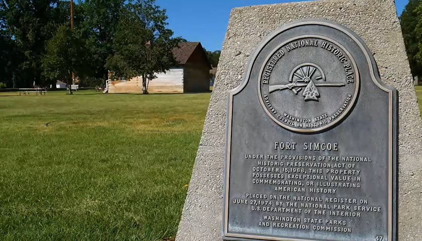 A comemorative stone and metal placque stands on the green grass grounds of Fort Simcoe Historical Park