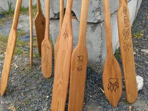 Paddles carved by fourth graders are brown and sitting against a stone structure.