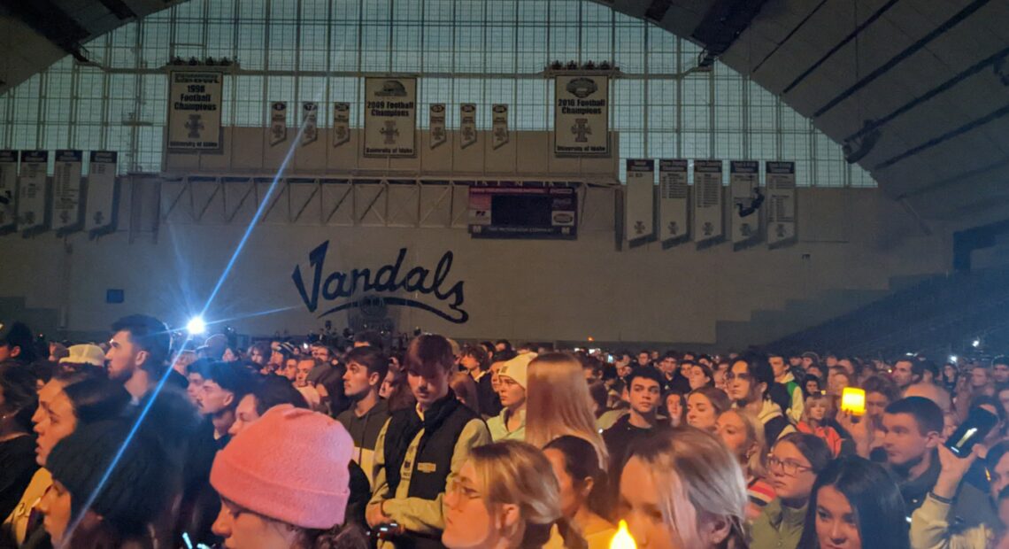 A crowd of hundreds of students hold up lights inside the Kibbie Dome with 'Vandals' written on the wall in black font in the distance.