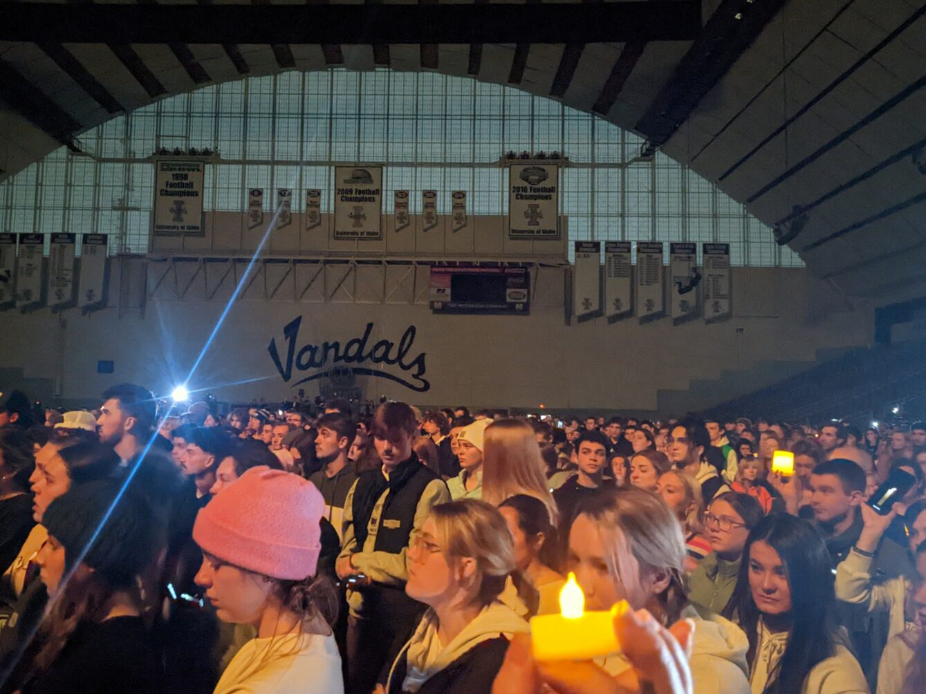 A crowd of hundreds of students hold up lights inside the Kibbie Dome with 'Vandals' written on the wall in black font in the distance.