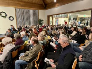 Audience members sit in wooden chairs in a church santuary.