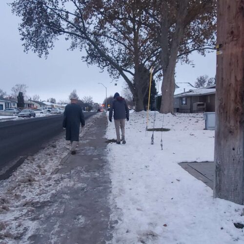 two people walking on an icy sidewalk one in the street